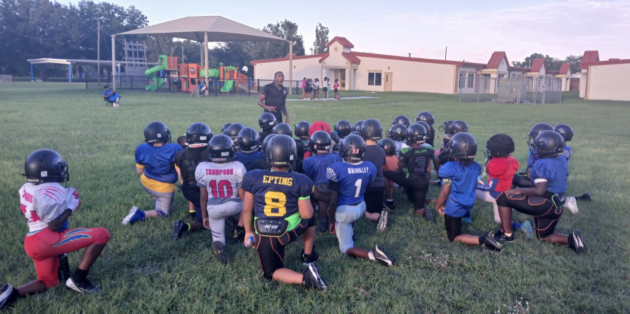 Jamisin Lacy mentoring a youth football team gathered around him on the field